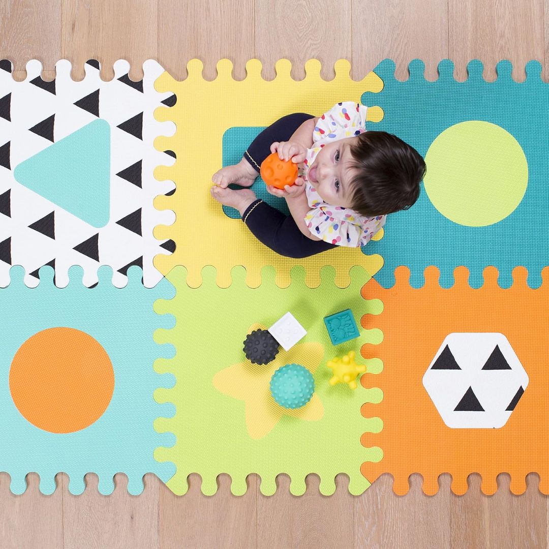 Child playing on a colorful foam puzzle mat with geometric shapes