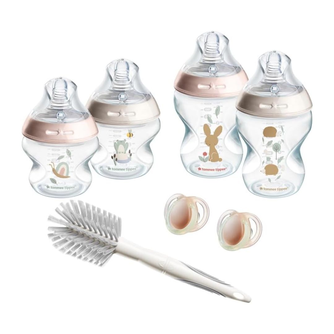Set of baby bottles with rose gold accents and a cleaning brush on a white background