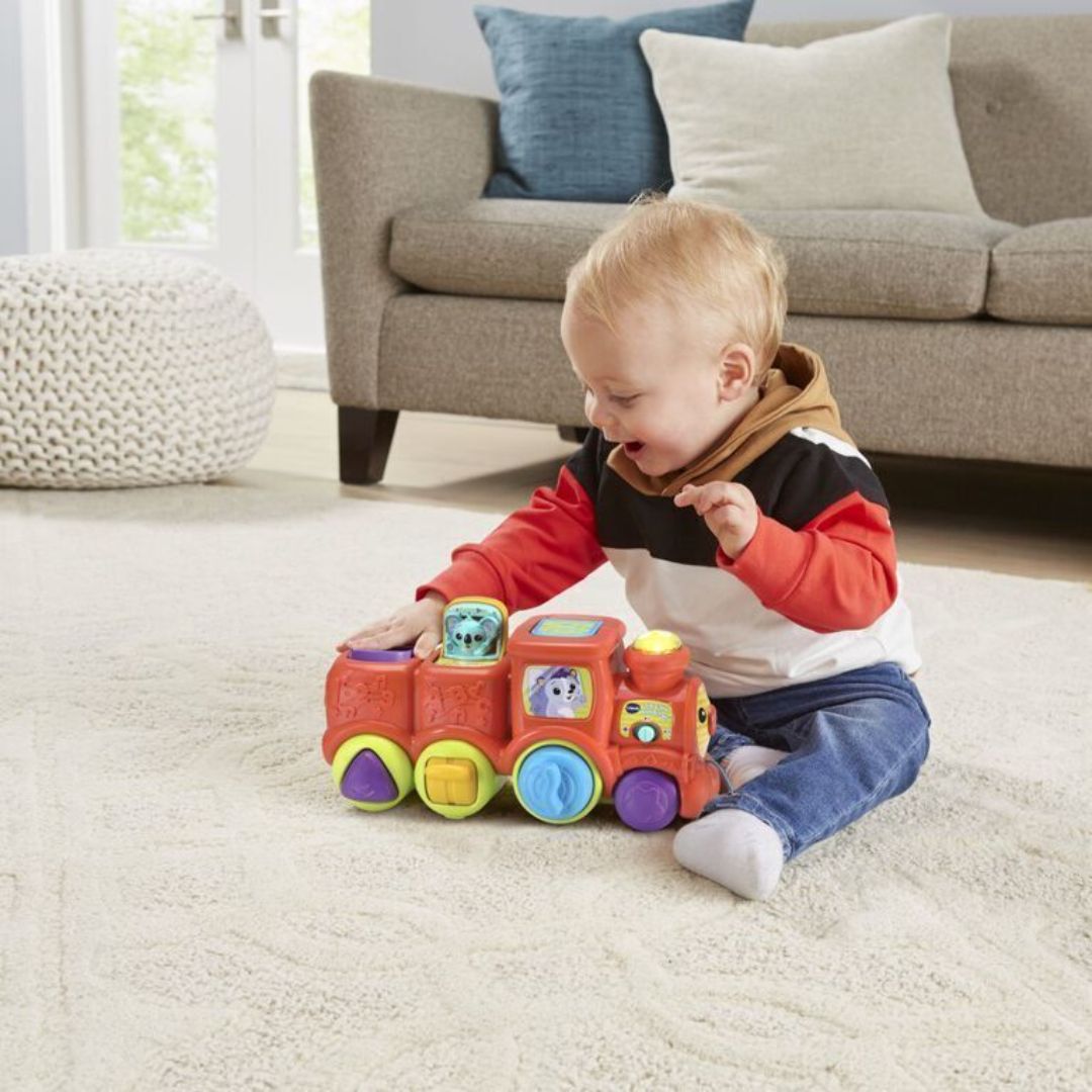 Child playing with a colorful toy train on a carpeted floor.