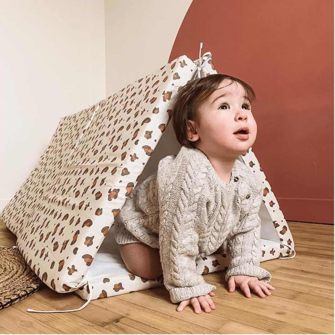 Child playing inside a leopard print play tent with a neutral background