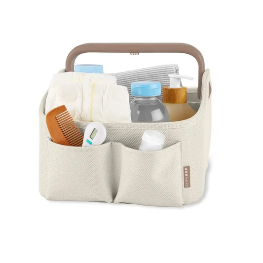 Skip Hop diaper caddy filled with baby essentials including diapers, wipes, lotion, a comb, a thermometer, and a bottle, showing its compartments and side pockets in use.