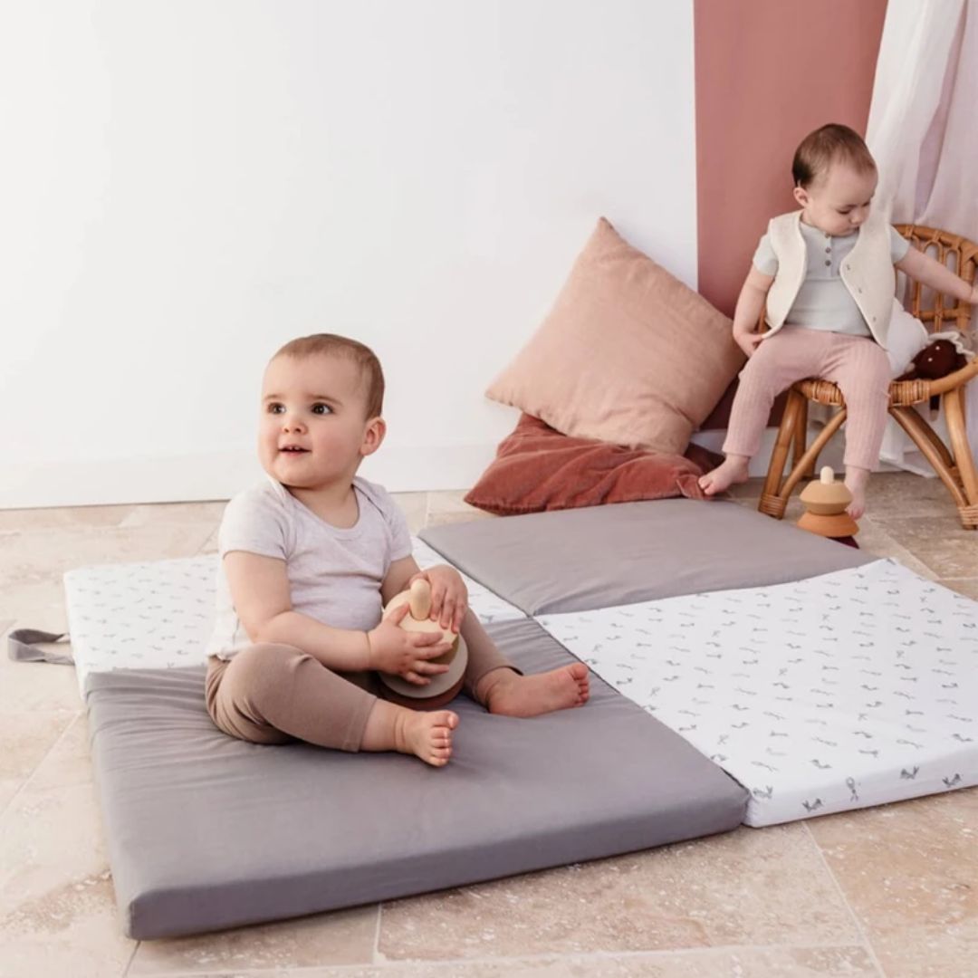 Candide Playmat Two babies playing on a soft play mat in a home setting.