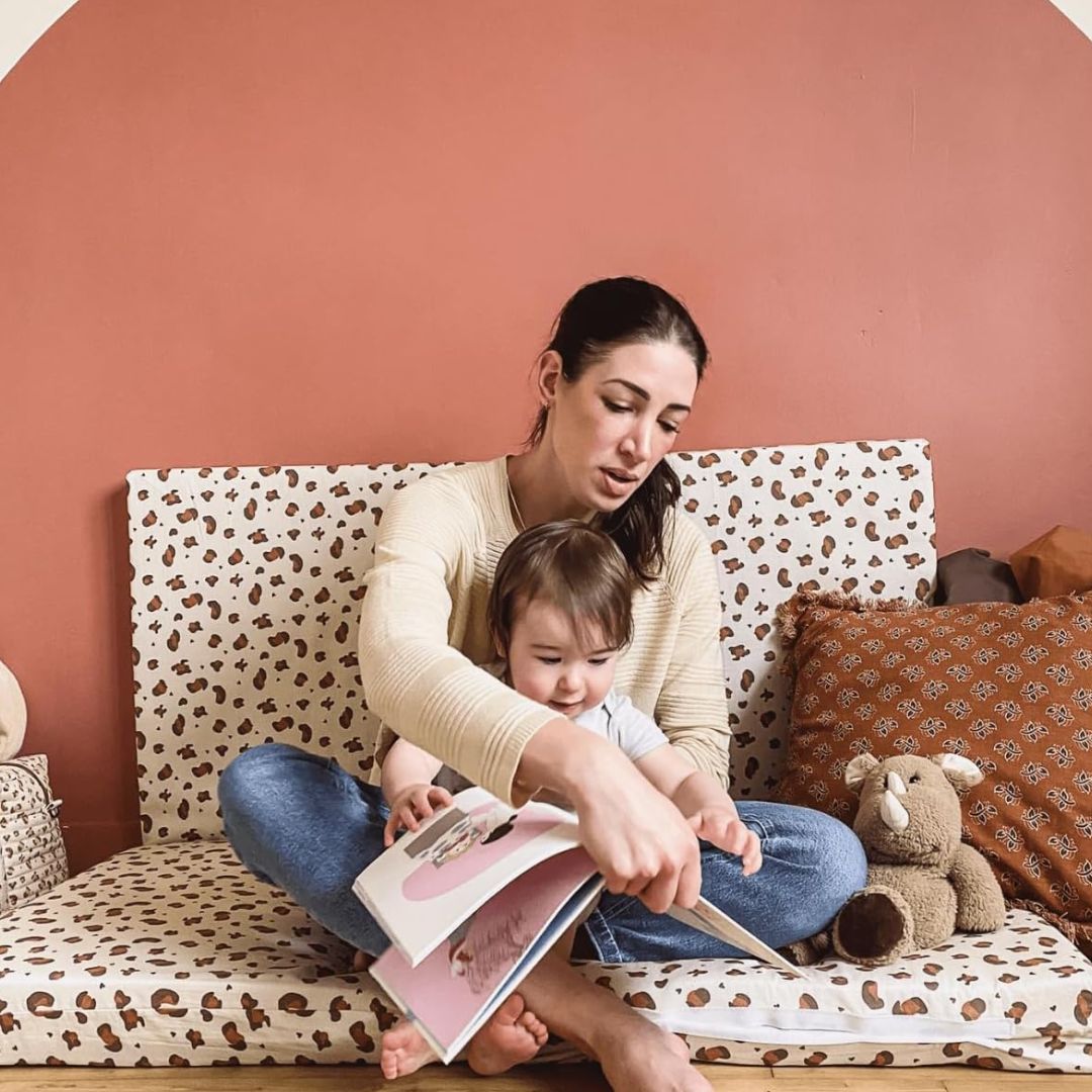 Woman reading a book to a child on a patterned Candide sofa with a pink wall.