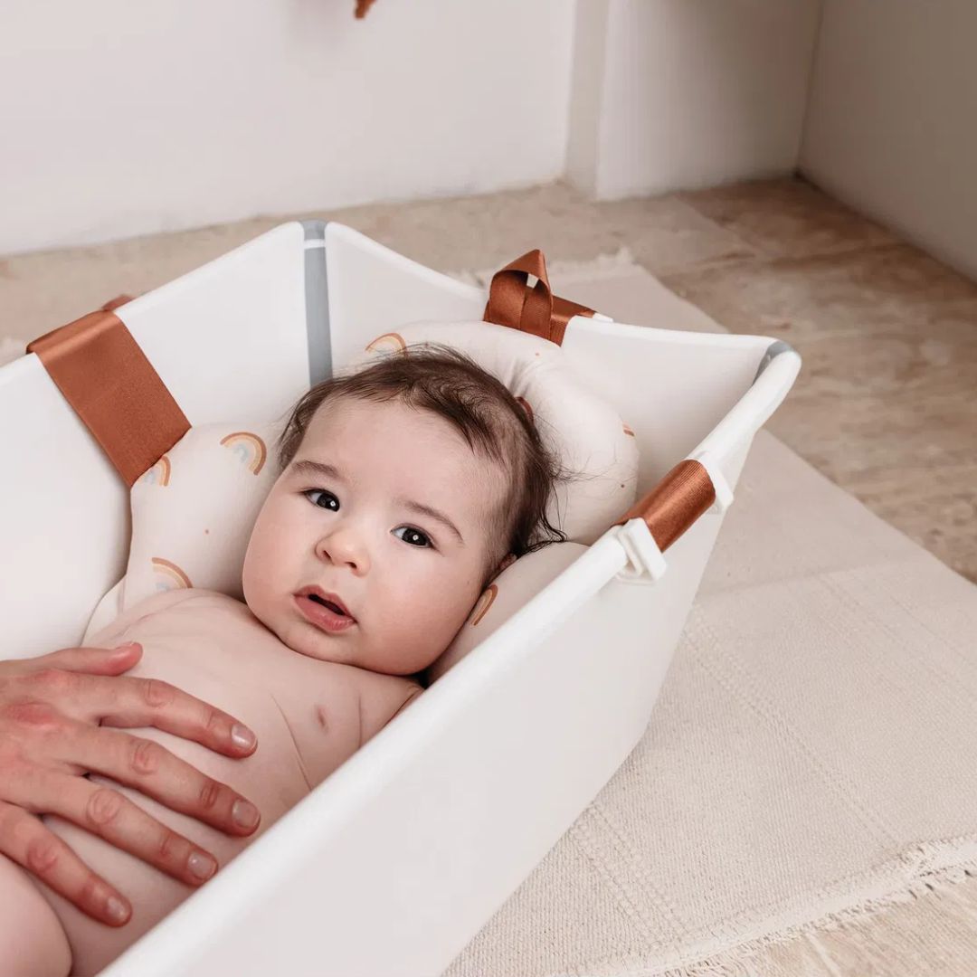 Baby lying in a white crib with brown bath pillow