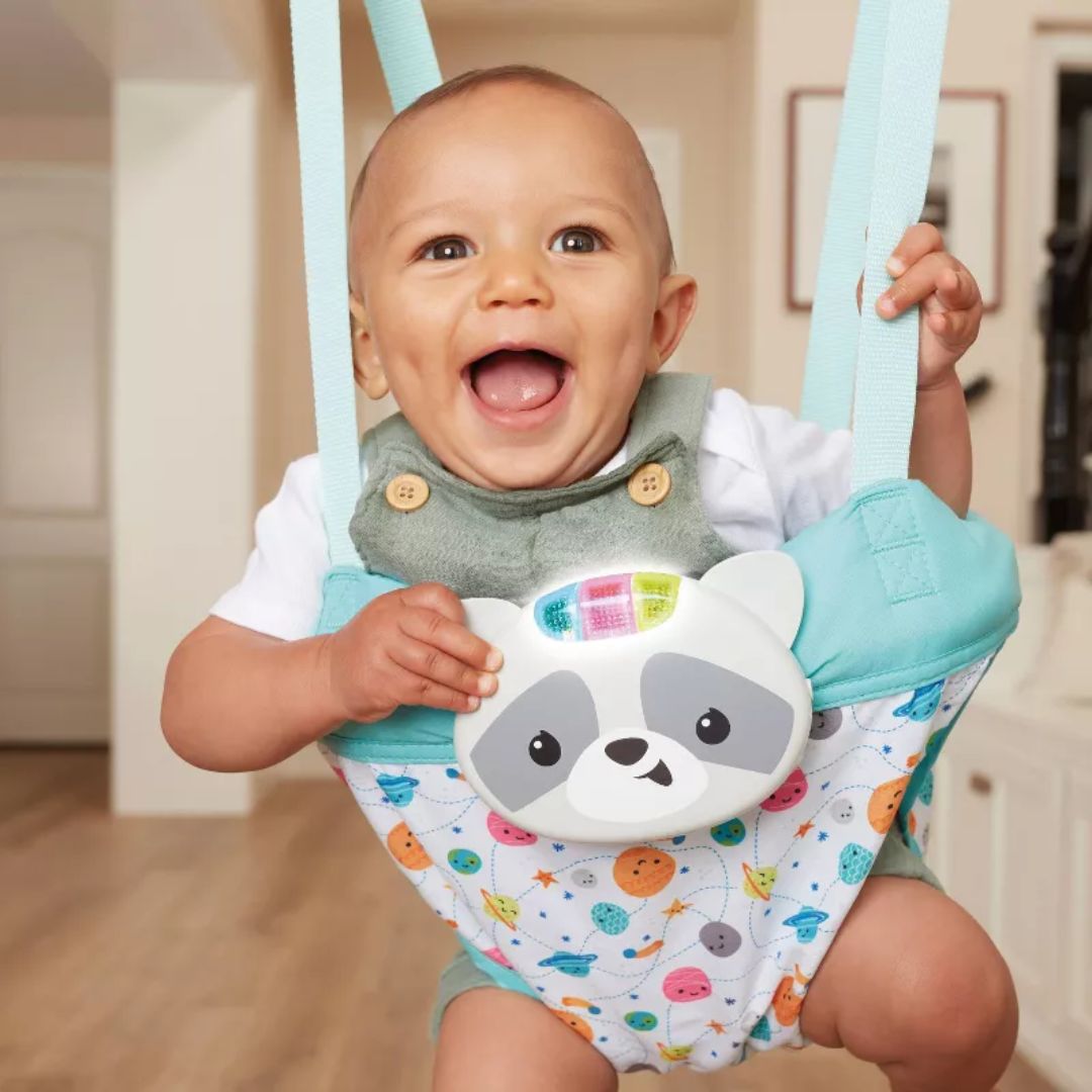 Baby in a colorful baby jumper with a raccoon design, smiling indoors.