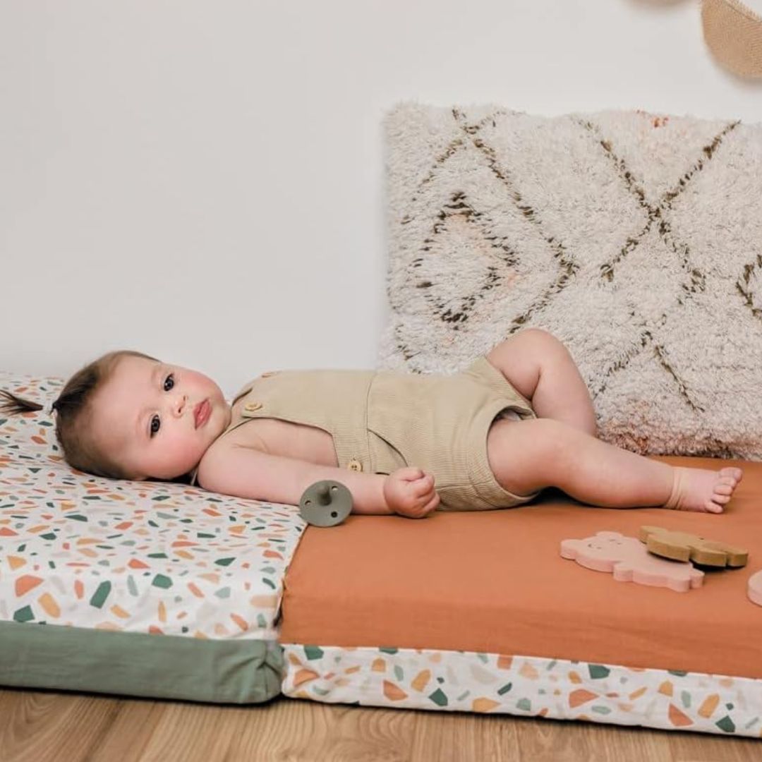 Baby lying on a colorful Candide play mat with a textured rug in the background