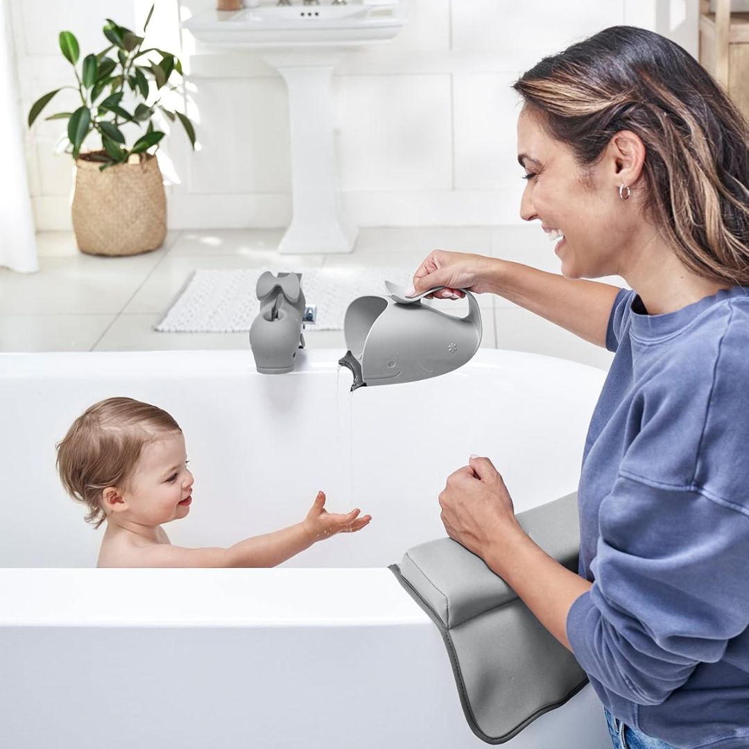 A smiling mother filling the Skip Hop whale-shaped bath rinser with water while a toddler sits in the bathtub nearby, with text listing care instructions: phthalate-free, dishwasher safe, hand wash in warm soapy water and air dry.