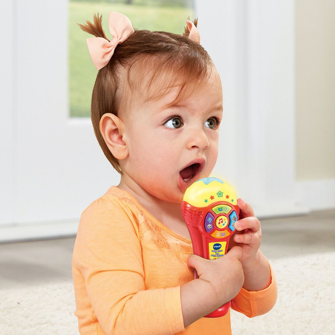 Baby holding a colorful toy vtech microphone indoors