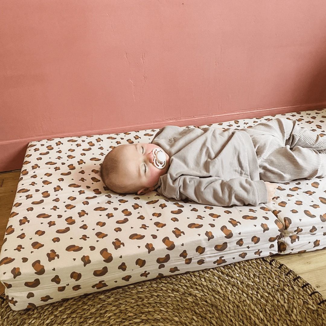 Baby lying on a leopard print mat against a pink wall