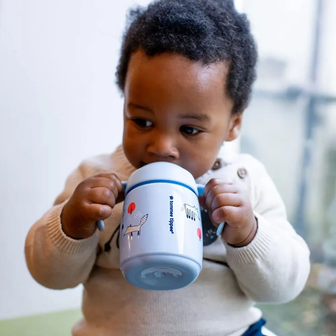 Child holding a blue Tommee Tippee Sippy Cup with a cartoon character on a blurred background