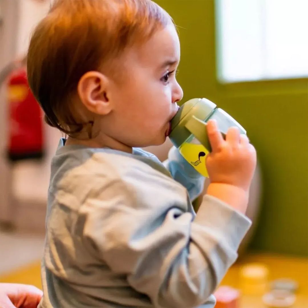 Baby holding a green Tommee tippee sippy cup indoors