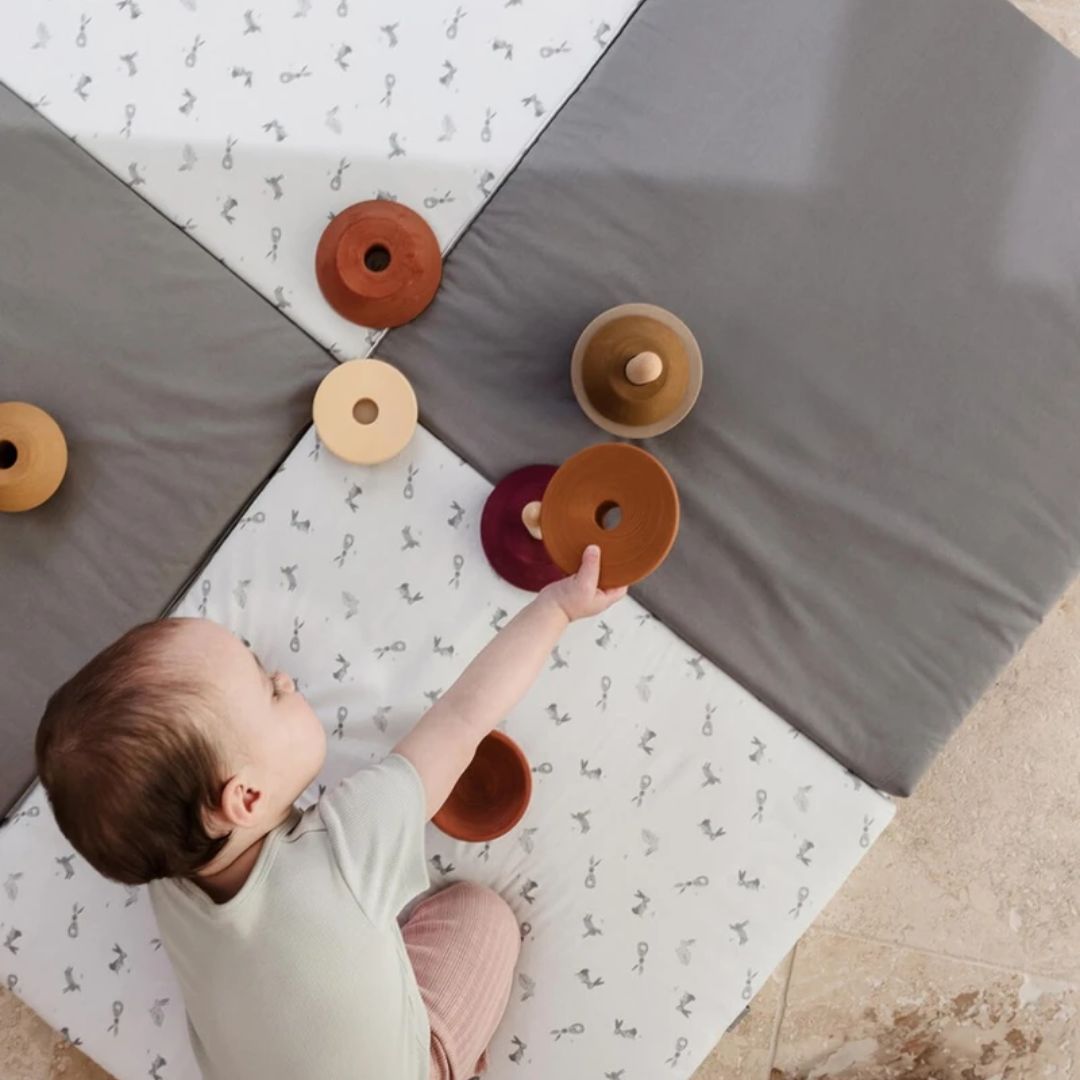 Candide Playmat Baby playing with wooden toys on a patterned floor