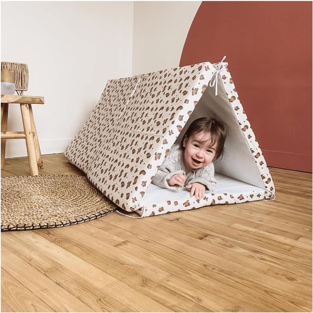 Child playing inside a candide patterned tent on a wooden floor.
