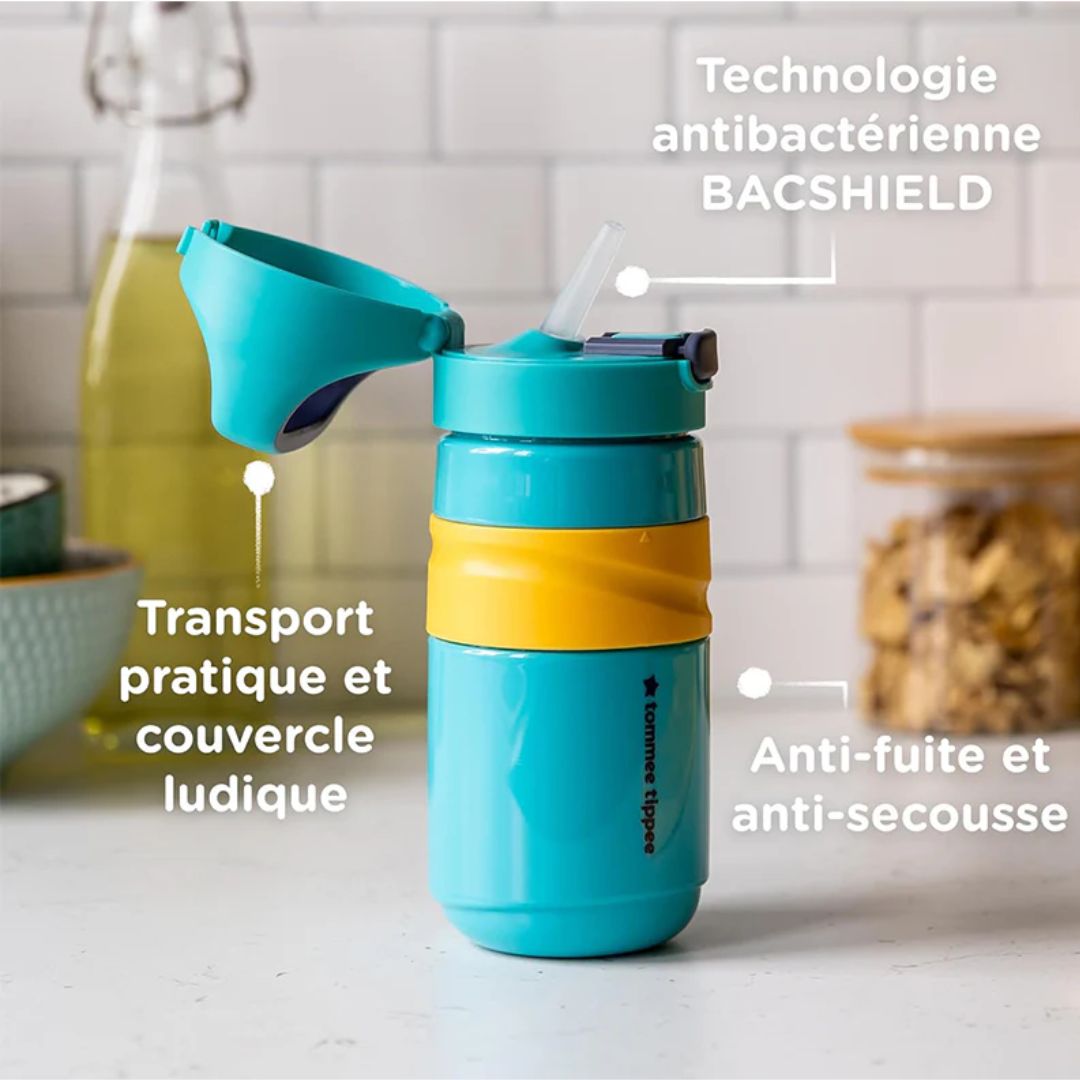Turquoise Tommee tippee water bottle with yellow band on a kitchen counter, featuring text about features.