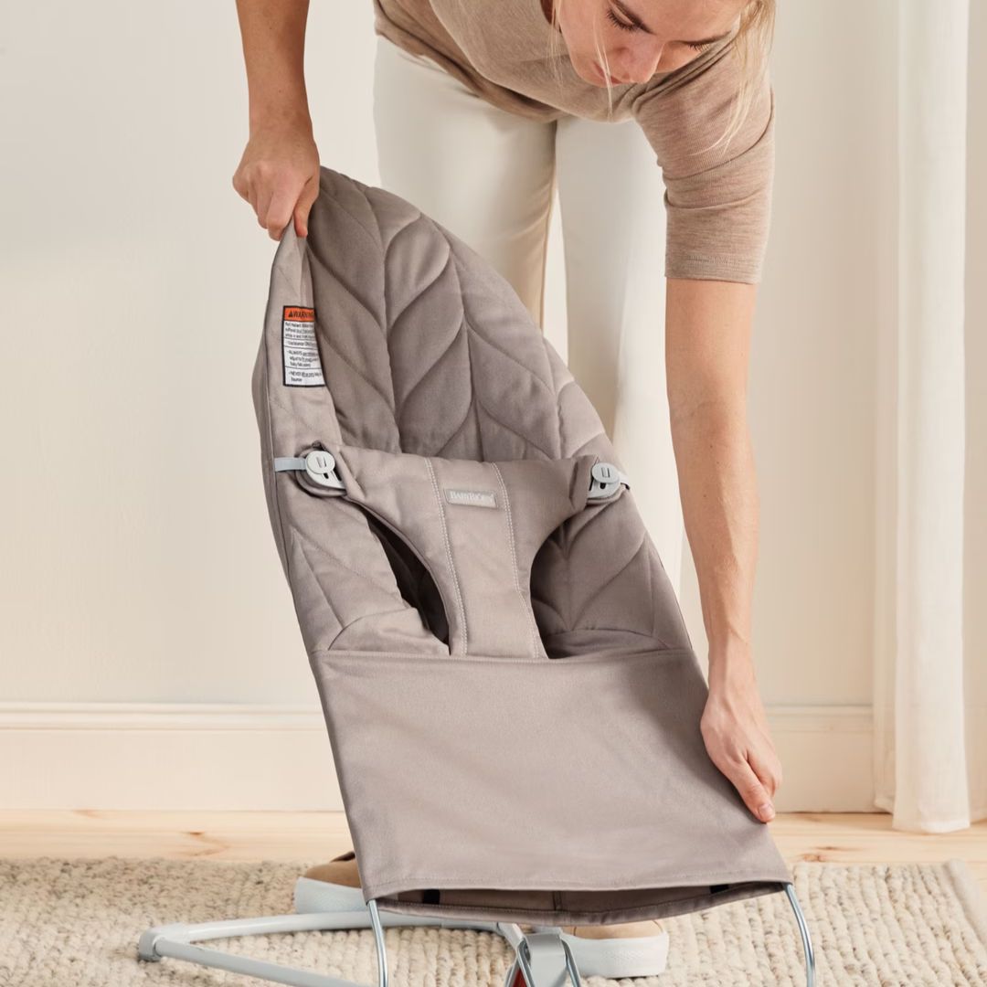 Person folding a BabyBjorn baby bouncer chair on a neutral background