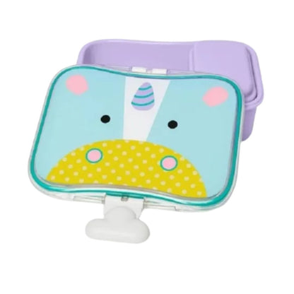 A baby Skip Hop feeding lunch box with a unicorn face design, featuring a light blue top, yellow polka-dot belly, pink ears, and a purple lid, shown on a white background.