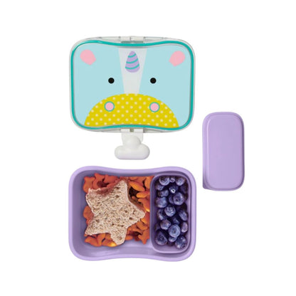 A children's Skip Hop lunch box set on a white background, featuring a light blue unicorn-themed lunch container with a white clip, a matching light purple lid, and an open purple compartment container holding a star-shaped sandwich, carrot sticks, and blueberries.