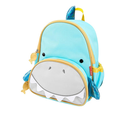 A Skip Hop light blue shark-shaped children's backpack with a white mouth and teeth, gold zipper trim, and small yellow fish accents, shown on a plain white background.