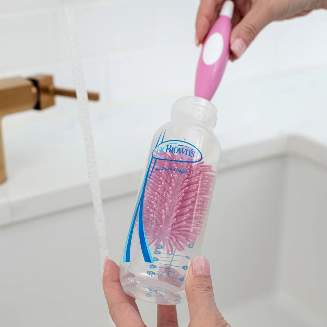 Person using a Dr Brown's  bottle brush with a pink handle under running water.