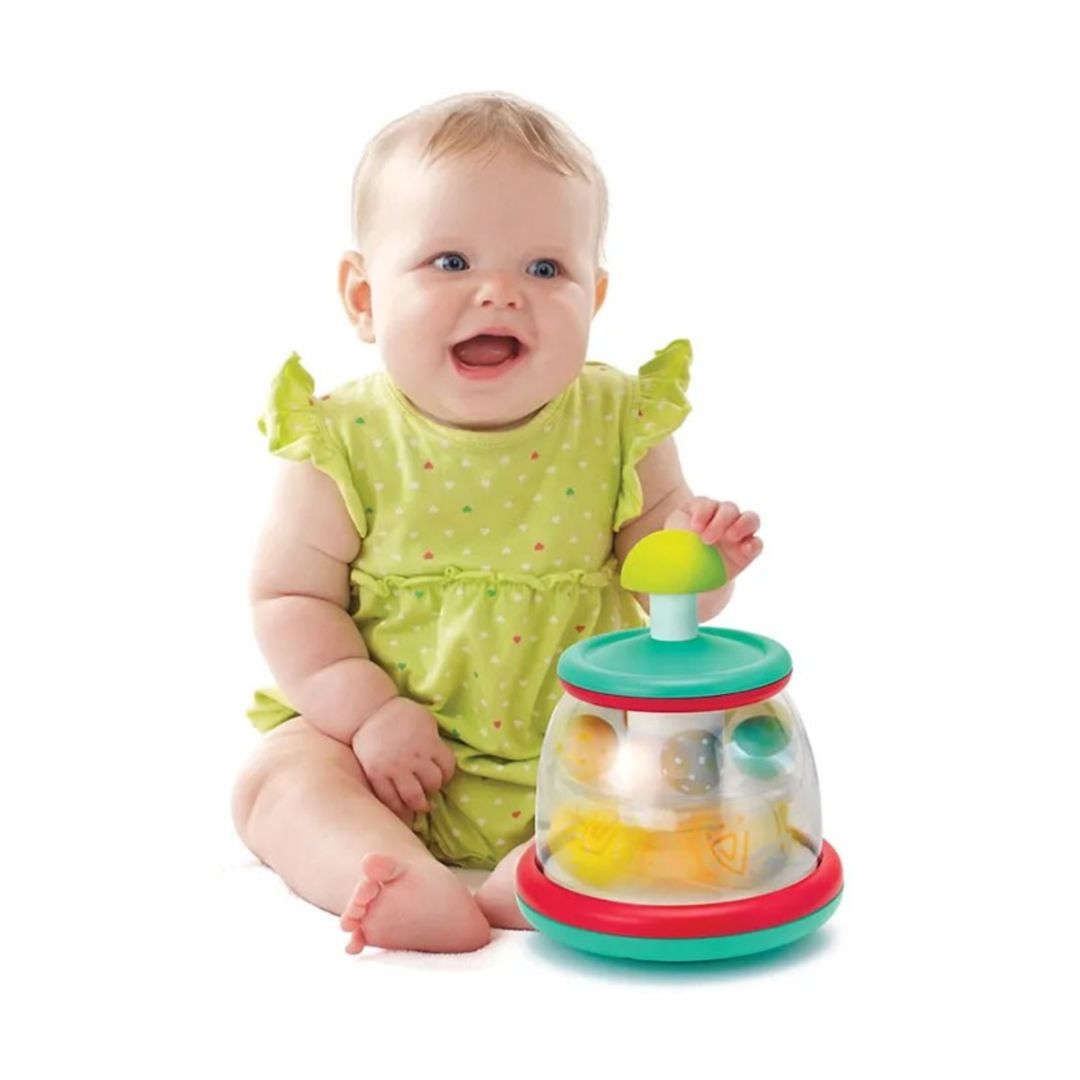 Baby in a green dress with a colorful infantino toy on a white background