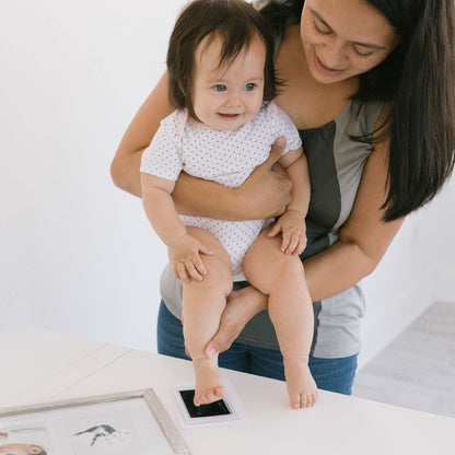 Woman holding a baby on a white surface with a Pearhead foot and handprint photo Cadre