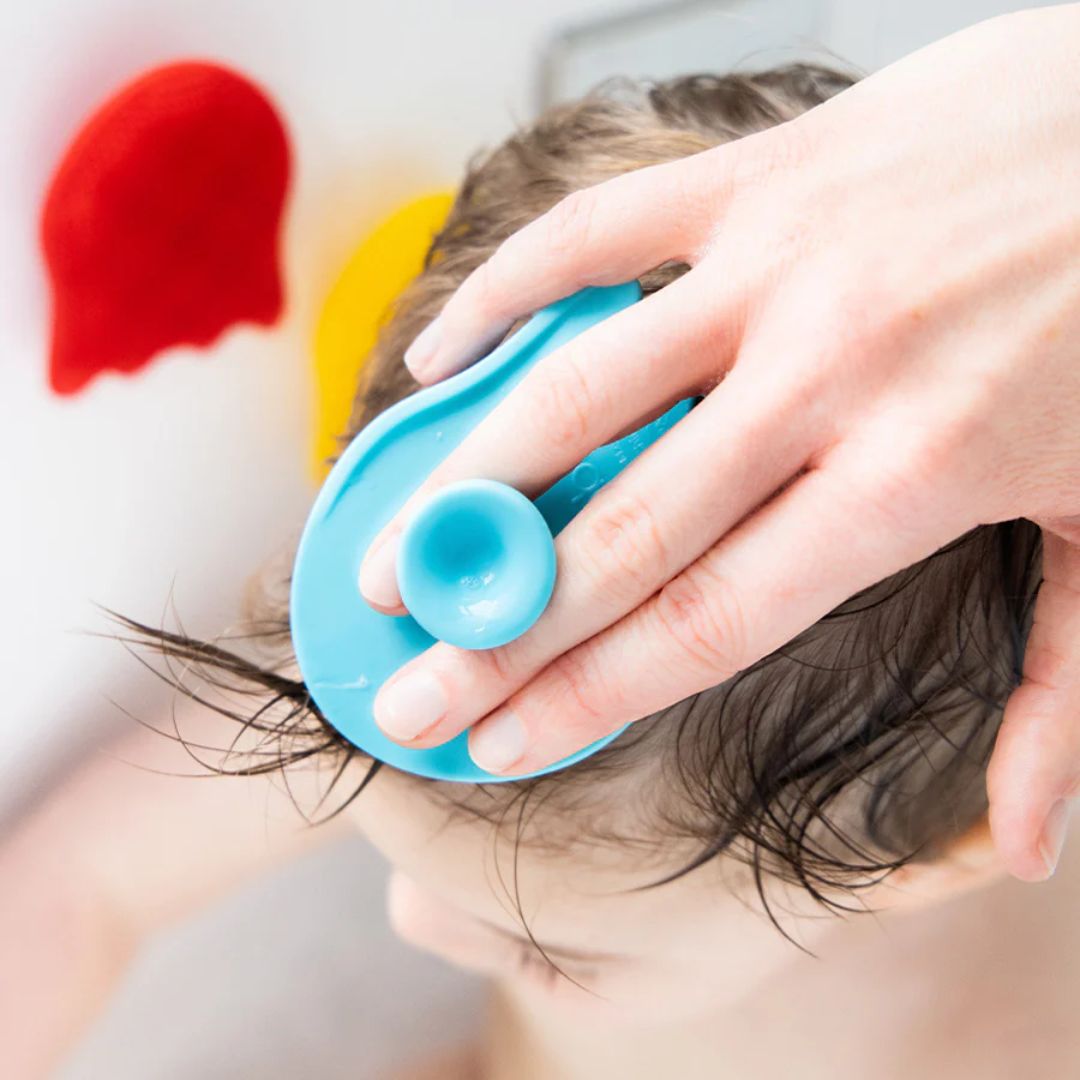 Person using an Ubbi blue baby silicone sponges on a child's hair with colorful hearts in the background