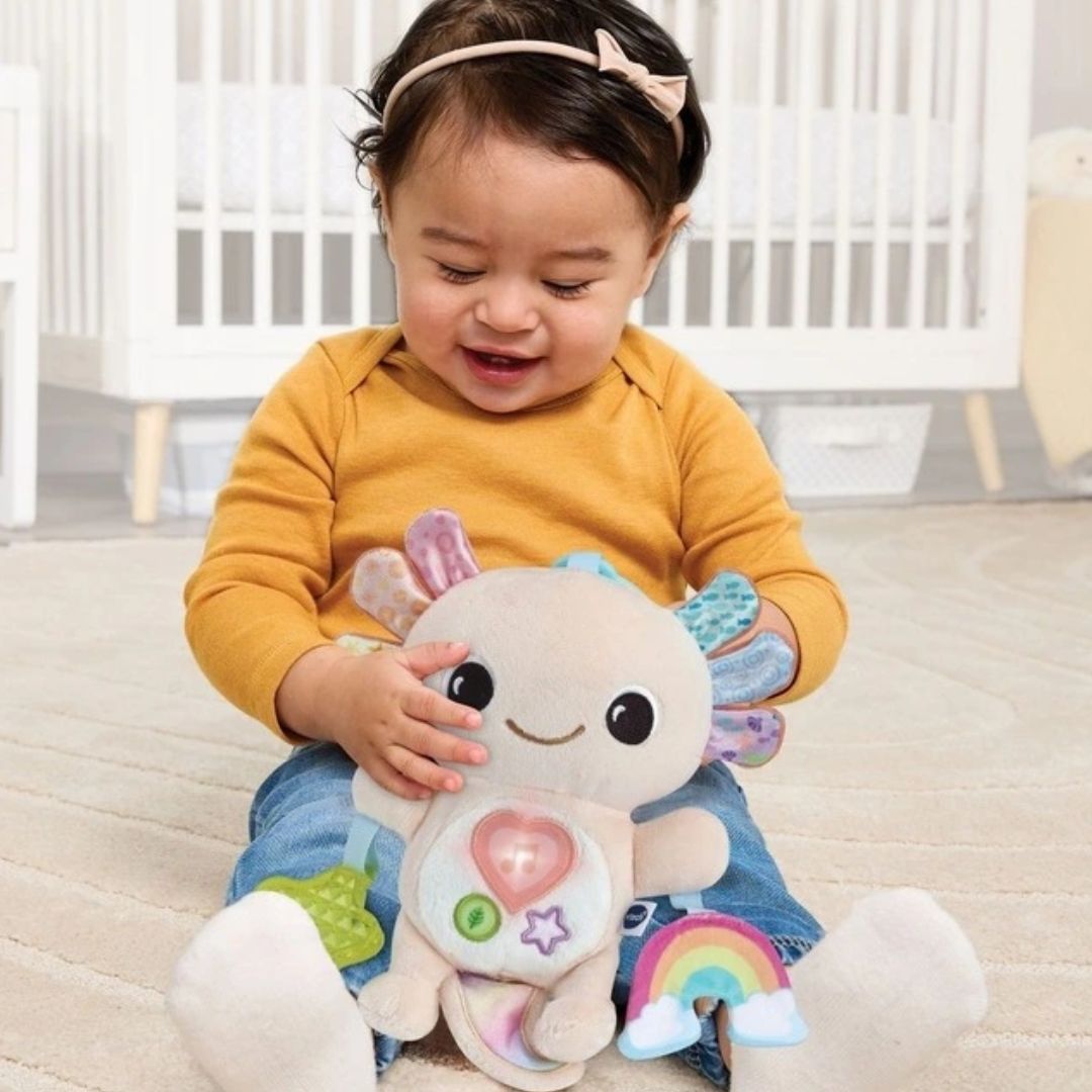 Vtech Child holding a plush toy with a smiley face in a crib setting