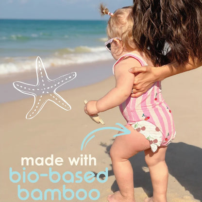 Child in a striped swimsuit being held by an adult on a beach with text 'made with bio-based bamboo'.