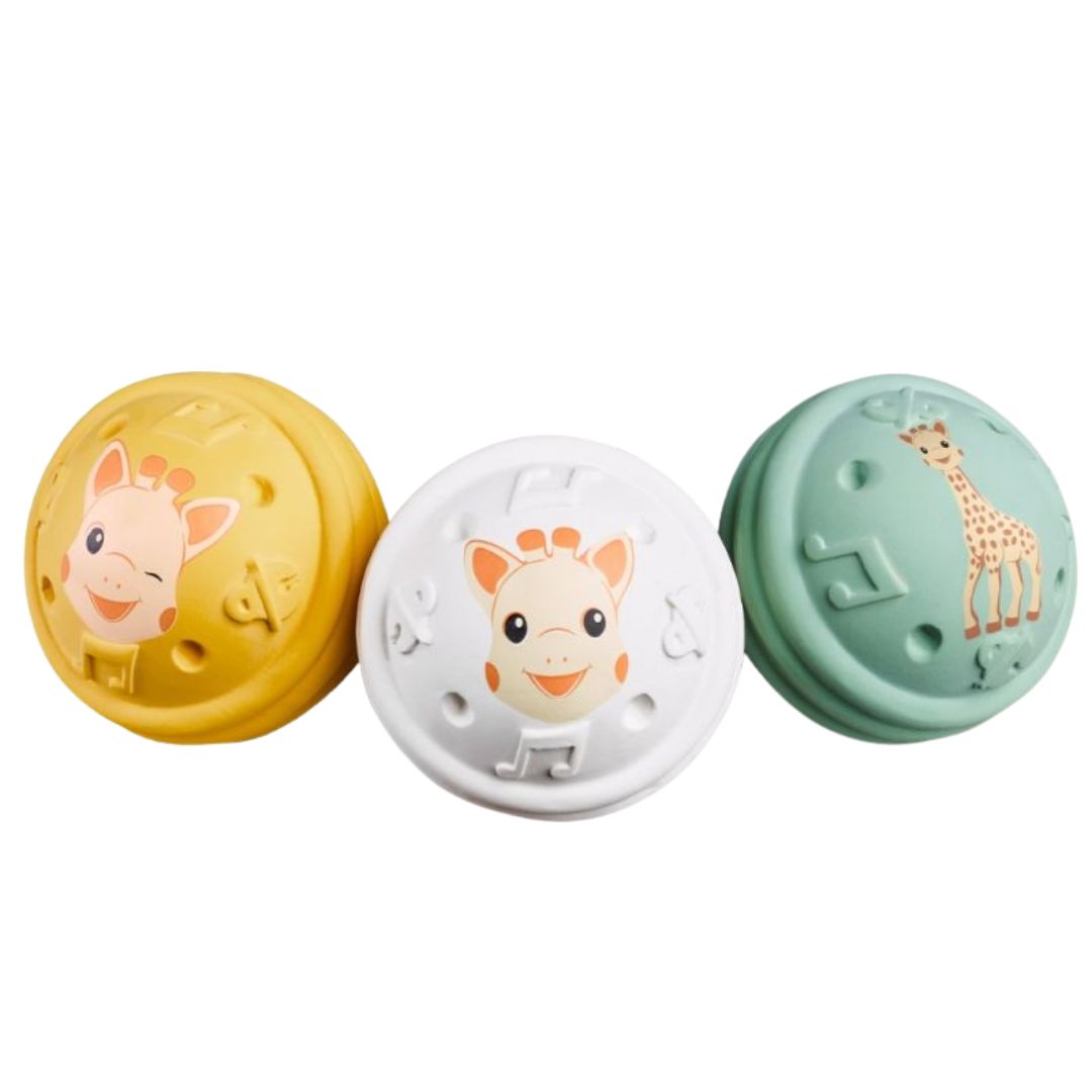 Three textured Sophie la Girafe musical balls in yellow, white, and green, each featuring a giraffe design, arranged side by side on a white background.