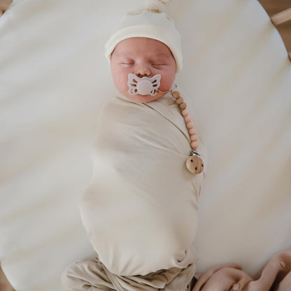 Newborn baby wrapped in a white blanket with a Frigg pacifier and teething ring.