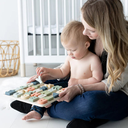 Woman and child playing with a Pearhead wooden puzzle on a light-colored floor.