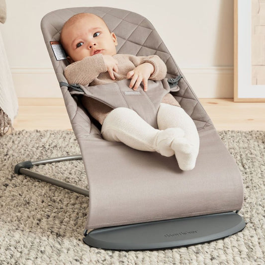 Baby Jorn Baby in a beige baby bouncer on a carpeted floor