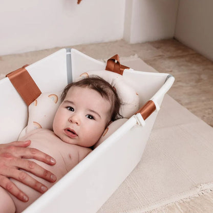 Baby lying in a white crib with brown bath pillow