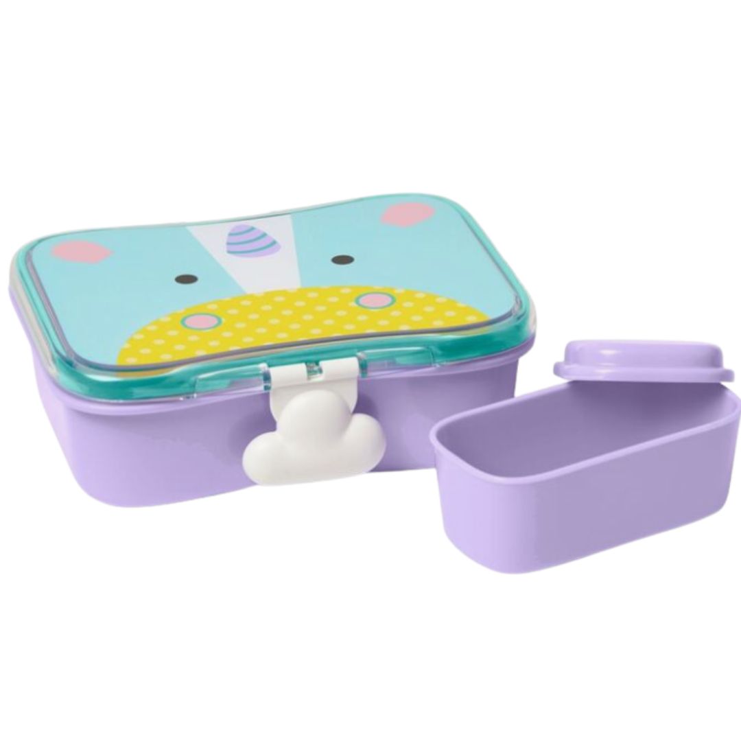 A pastel purple bento Skip Hop lunch box with a lid featuring a cartoon animal face in light blue, yellow, and pink, shown next to its detached lid on a white background.