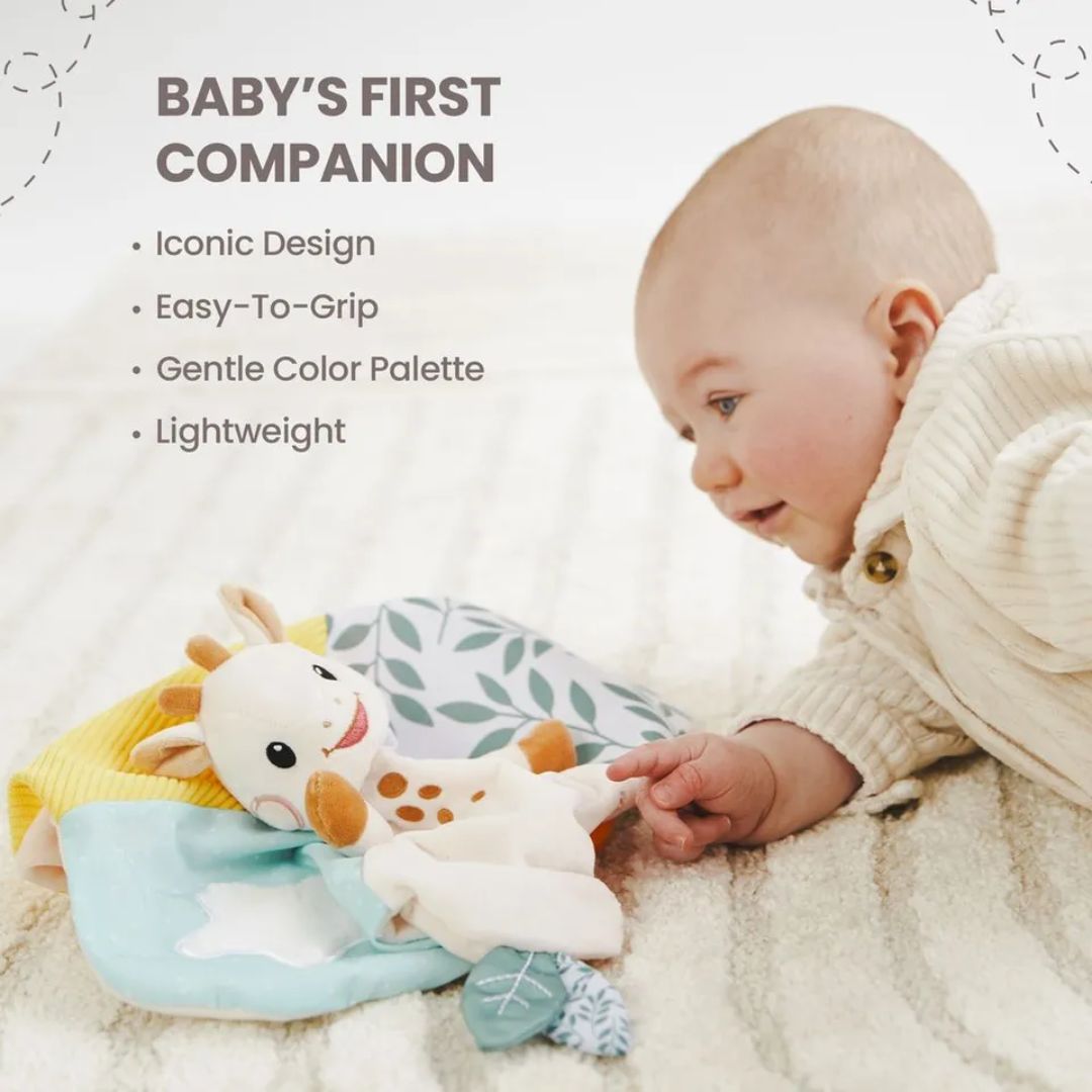 A baby lying on their stomach reaching toward the Sophie la Girafe comforter, with text listing features: Iconic Design, Easy-To-Grip, Gentle Color Palette, Lightweight.