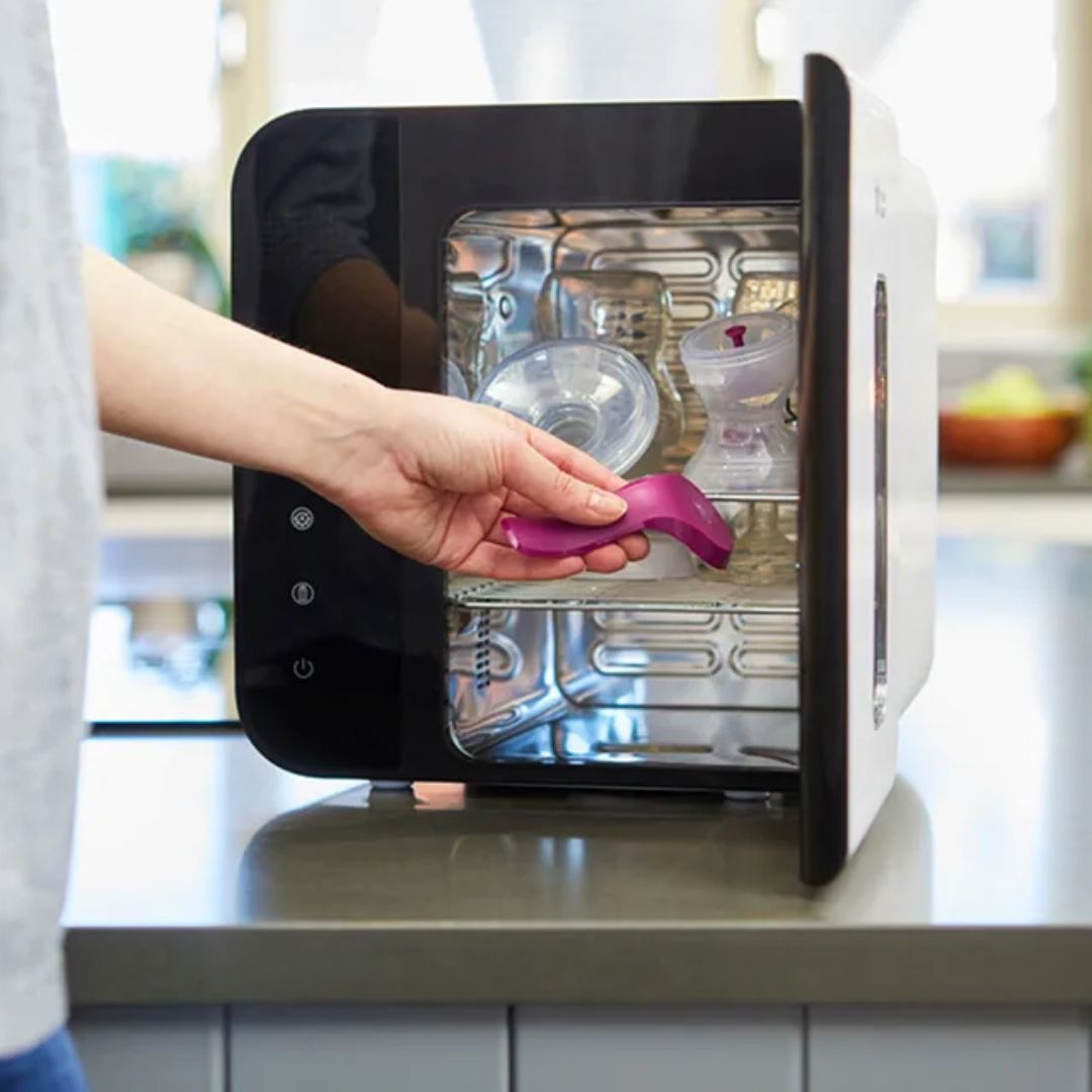 Person placing a purple spoon into an open Tommee tippee sterilizer.