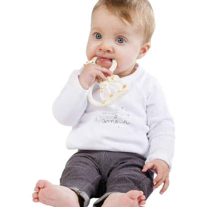 A baby in a white top chewing on the Sophie la Girafe teething ring, holding it to their mouth with both hands.