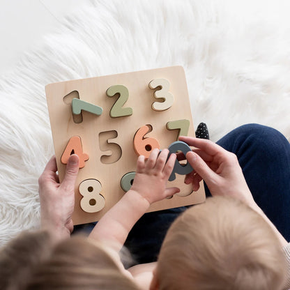 Child playing with a Pearhead wooden number puzzle on a soft white surface