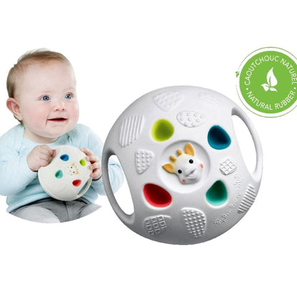 A baby in a light blue top holding and smiling at the Sophie la Girafe Senso Ball, with a close-up of the ball's textured, colorful surface and a natural rubber badge shown beside it.