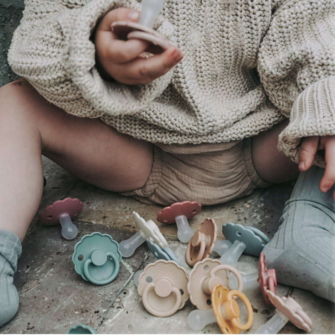 Child playing with colorful Frigg pacifiers on a concrete surface