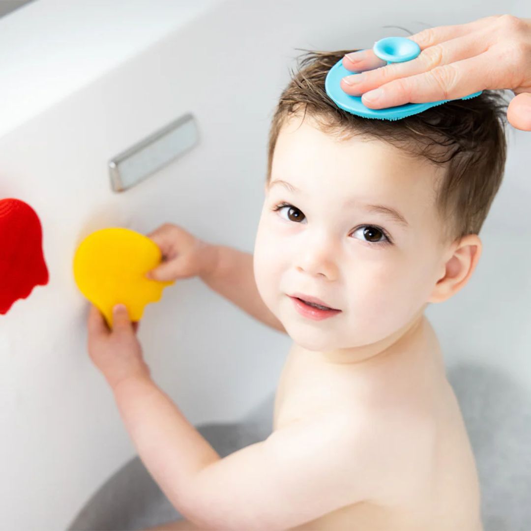 Child playing with colorful Ubbi silicone bath sponges in a bathtub