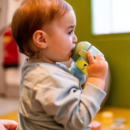 Baby holding a green Tommee tippee sippy cup indoors