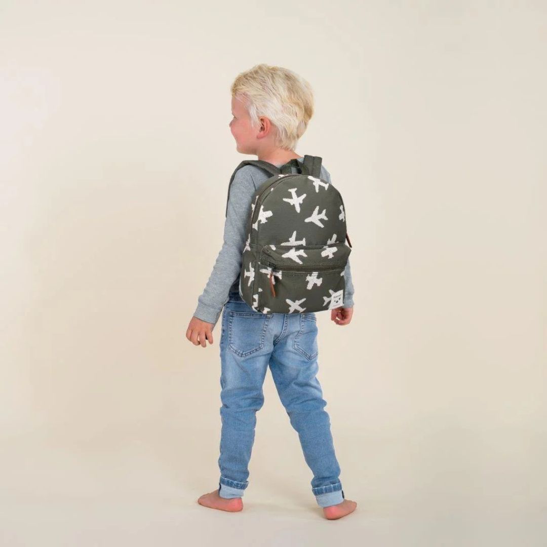 Child wearing a backpack with airplane pattern on a plain background