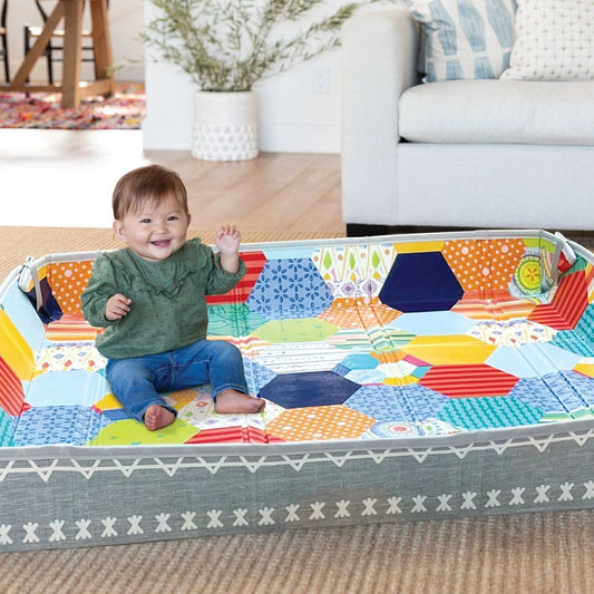 Child sitting on a colorful Infantino play mat in a living room