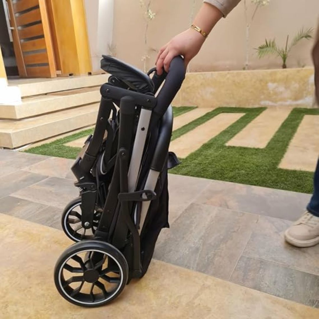 Person holding a folded Kidilo black stroller on a patio