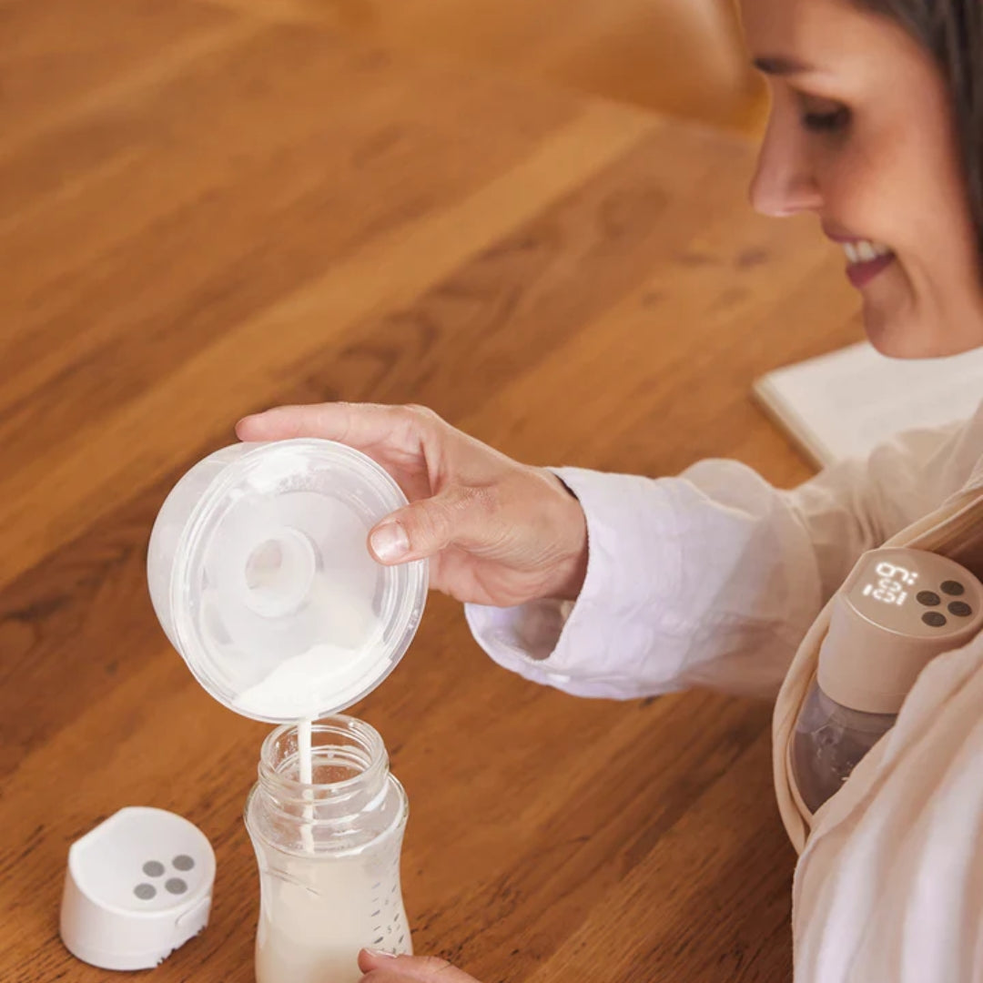 Woman using a Momcozy  breast pump with a bottle on a wooden floor