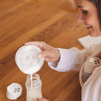 Woman using a Momcozy  breast pump with a bottle on a wooden floor