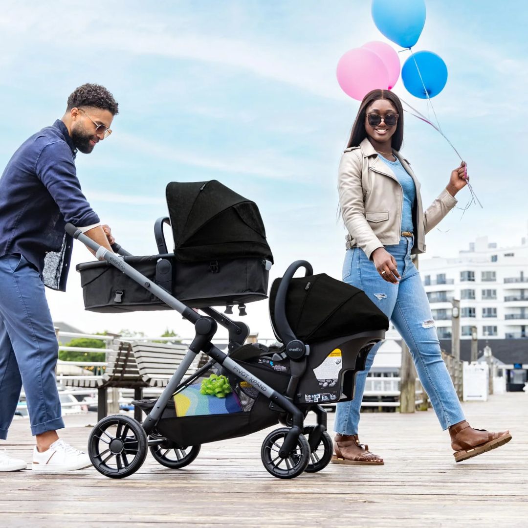 Man pushing an Evenflo stroller with a woman holding balloons on a wooden deck.