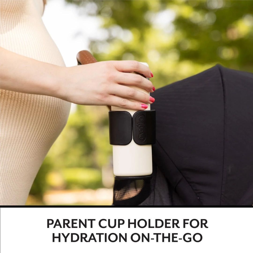 Person holding a cup with a parent cup holder against a blurred outdoor background