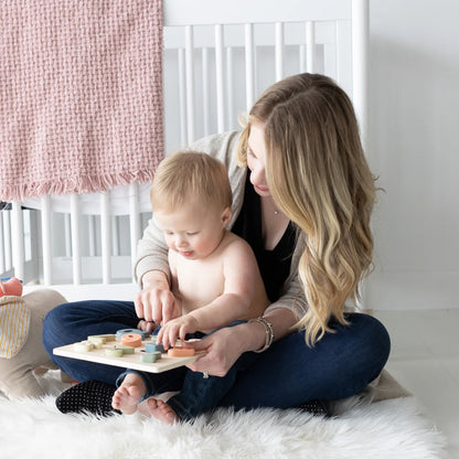 Woman and child playing with a Pearhead wooden toy on a white rug in a nursery.